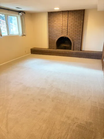 Spacious room featuring a brick fireplace with an arched opening and raised hearth
