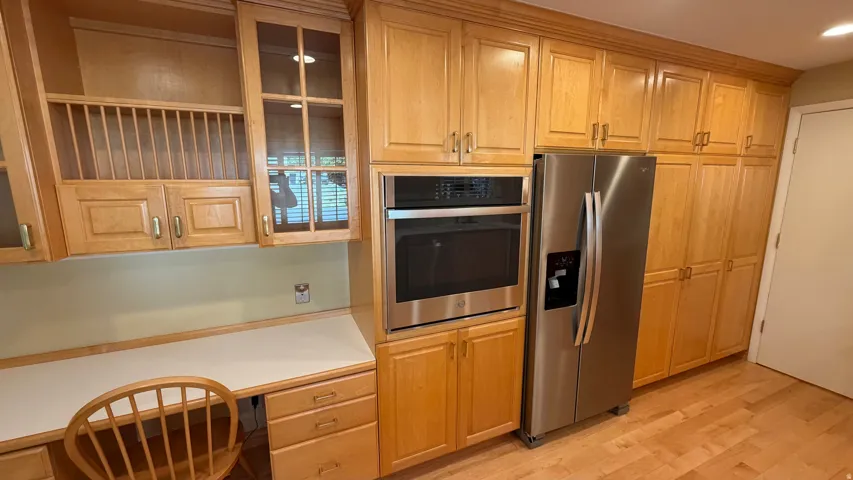 Kitchen featuring extensive wood cabinetry, stainless steel appliances including a built-in oven and refrigerator, an integrated desk area with storage, and wood-finish flooring