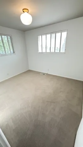 Room featuring neutral-toned carpeting, white walls, and two windows with blinds