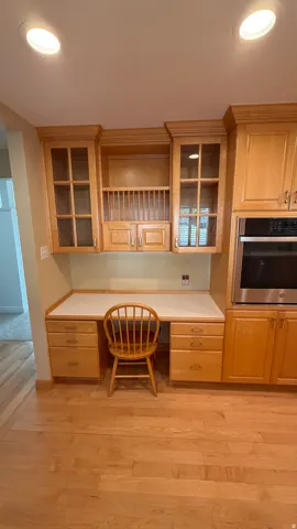 Built-in desk area featuring light wood cabinetry with glass-front uppers, a plate rack, and ample drawer storage