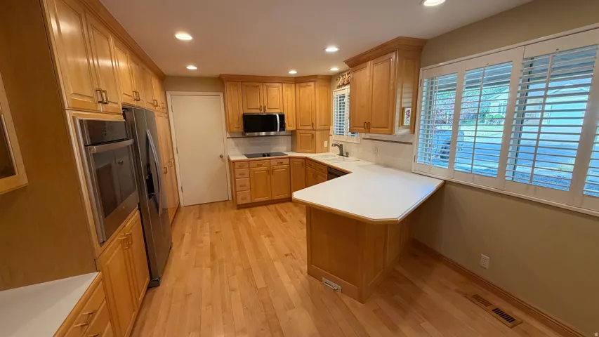 Kitchen featuring wood-finish flooring, extensive cabinetry, stainless steel appliances, white countertops, and plantation shutters