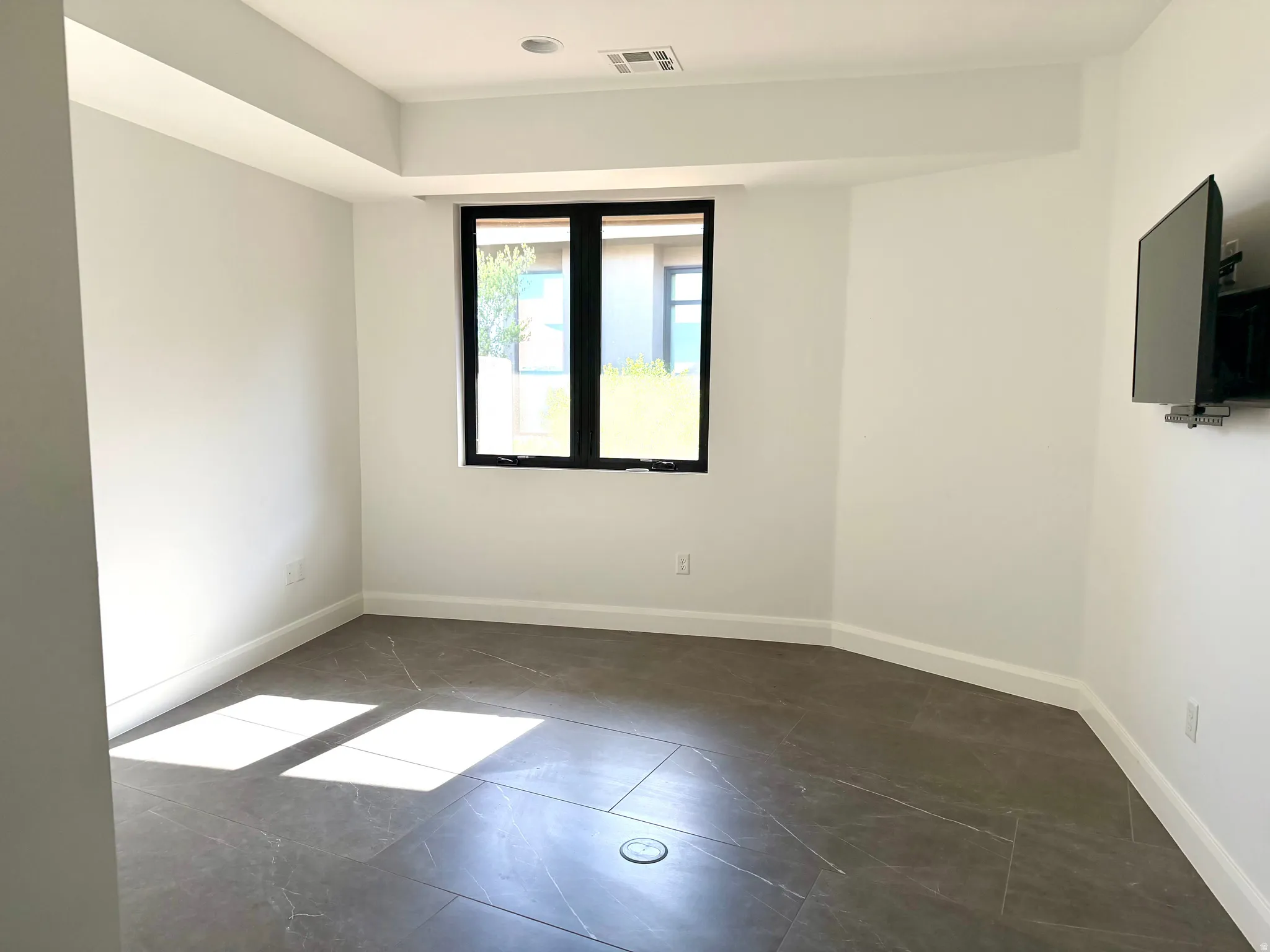 Room featuring large format tile flooring, a prominent black-framed window, recessed ceiling lights, and crisp white baseboards