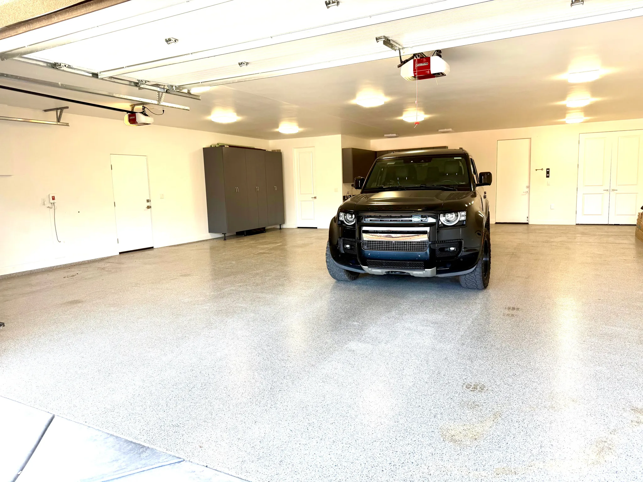 Spacious garage featuring a speckled epoxy floor, multiple overhead lights, automatic garage door openers, and built-in storage cabinetry