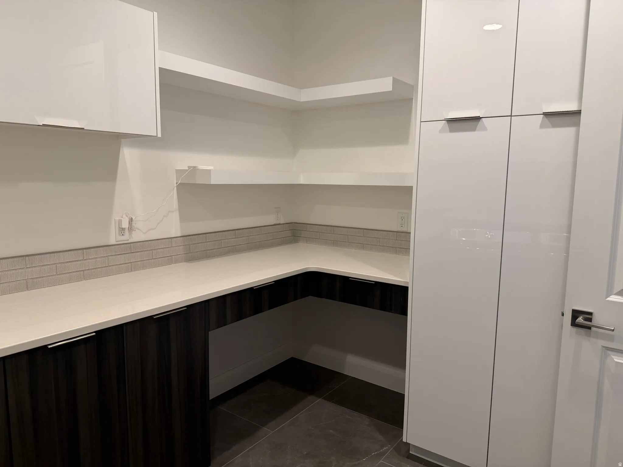 Modern kitchen pantry featuring white upper cabinetry and dark wood-finish lower cabinetry, light-toned countertops, and an integrated subway tile backsplash