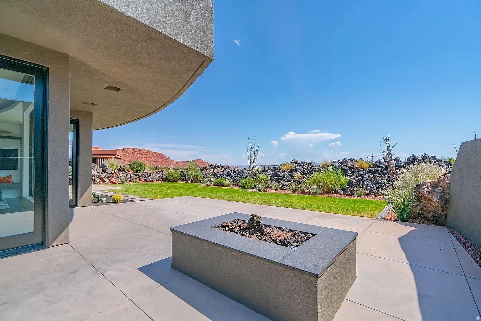 Expansive patio featuring a built-in fire pit with decorative rocks, concrete surfacing, and direct access to the interior via large glass doors