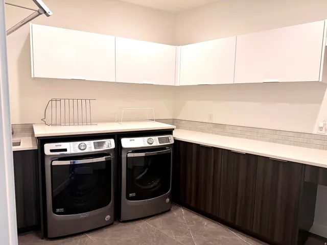 Laundry area featuring white upper cabinetry, dark wood-finish lower cabinetry, white countertops, and a gray tile backsplash