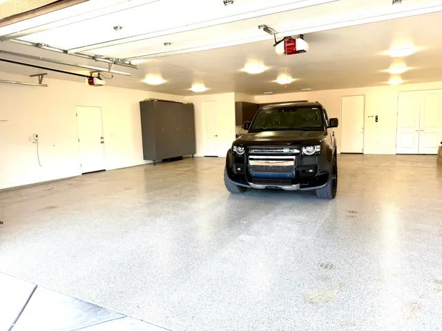 Spacious garage featuring a speckled epoxy floor, multiple overhead lights, automatic garage door openers, and built-in storage cabinetry