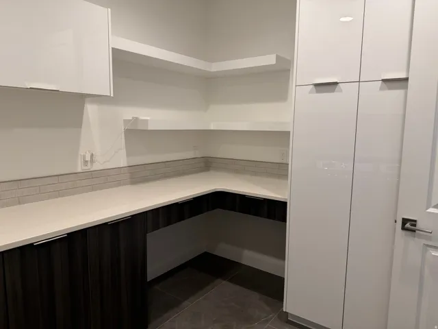 Modern kitchen pantry featuring white upper cabinetry and dark wood-finish lower cabinetry, light-toned countertops, and an integrated subway tile backsplash