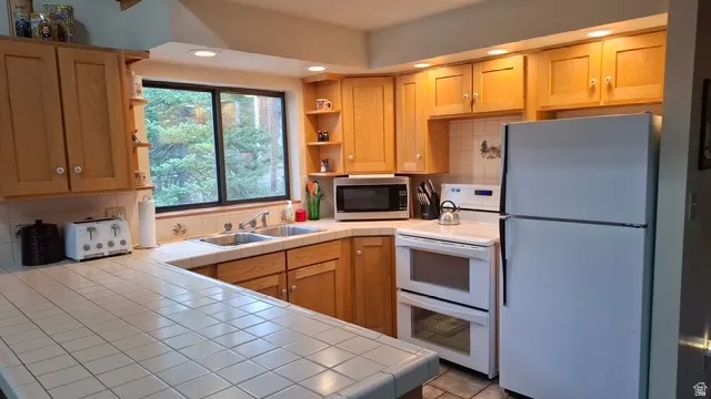Kitchen featuring tile countertops, solid surface range with double ovens, tile flooring, white appliances and a view of the great outdoors from the window above the sink