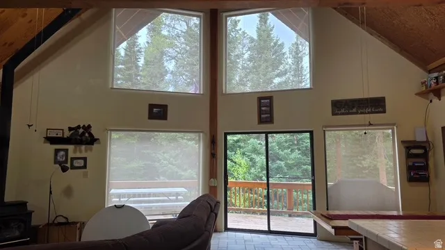 Vaulted ceiling with exposed wood beams, featuring multiple angular floor-to-ceiling windows and glass sliding doors out to a large, uncovered deck