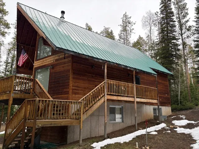 Wood-sided cabin featuring a green metal roof and a raised wood deck