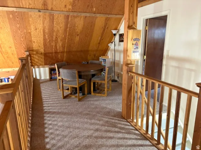 Carpeted loft area featuring wood paneling on vaulted ceilings, a round gaming table, and a wood railing overlooking the main level great room