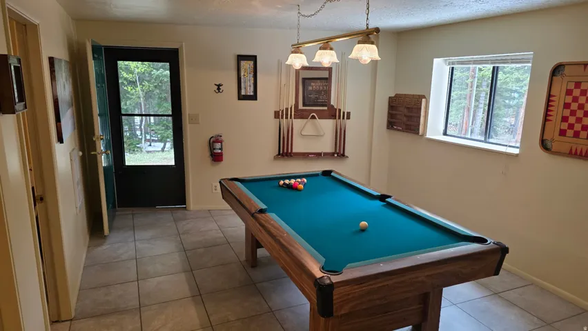 Rec room with outside entry at ground level featuring a pool table with cue rack, tile flooring and an abundance of natural light