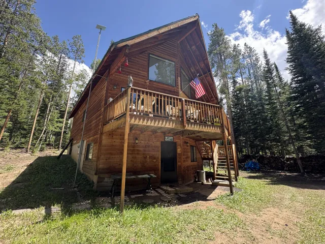 Wood-sided cabin featuring an elevated deck with wood railing, a gabled roofline, and a lower-level open area