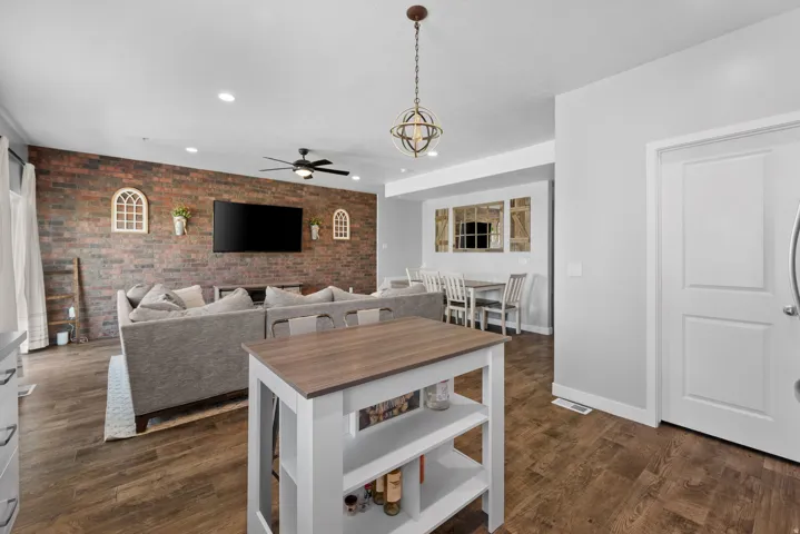 Open-concept living space featuring wood-finish flooring, a brick accent wall, and recessed lighting