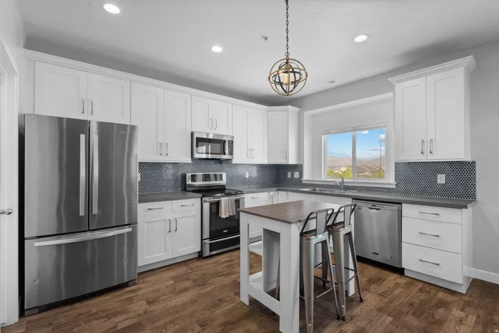 Modern kitchen featuring white shaker cabinetry, stainless steel appliances, dark countertops, a mosaic tile backsplash, and wood-finish flooring