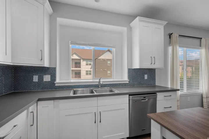Contemporary kitchen featuring white cabinetry, dark countertops, and a full-height penny tile backsplash