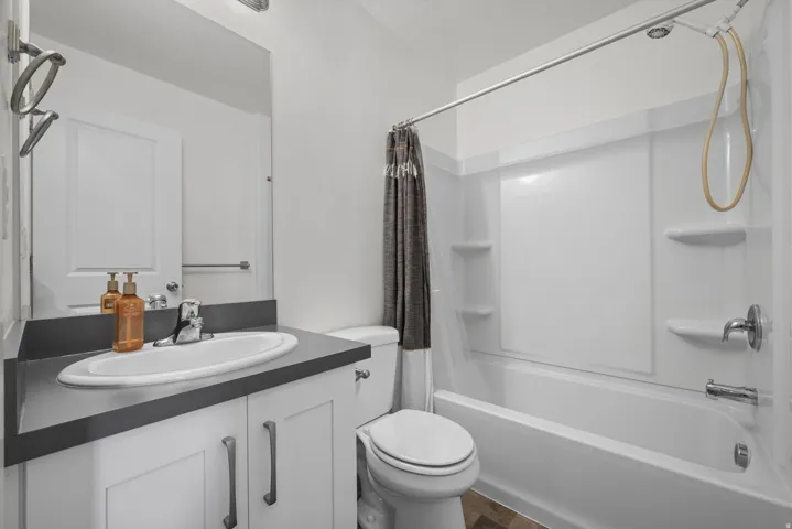 Bathroom featuring a white vanity with a dark countertop, an integrated sink, and white cabinetry with brushed nickel hardware