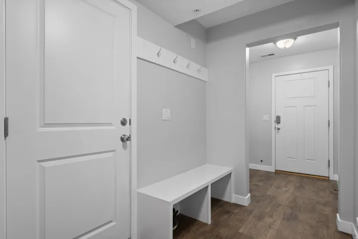 Entryway featuring wood-finish flooring, light gray walls, a white built-in bench, and a white coat rack with five hooks