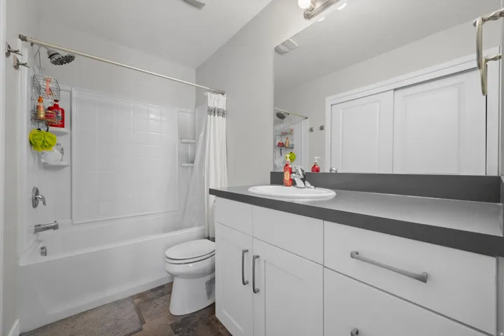 Contemporary bathroom featuring a white vanity with modern hardware, a countertop with an integrated sink, a full-width mirror, and a white subway-tiled bathtub/shower combination