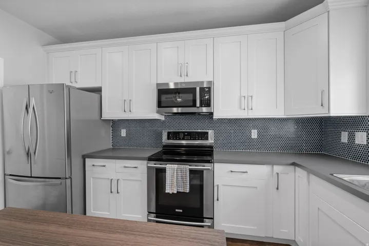 Modern kitchen featuring white shaker cabinetry, stainless steel appliances, dark penny tile backsplash, and solid surface countertops