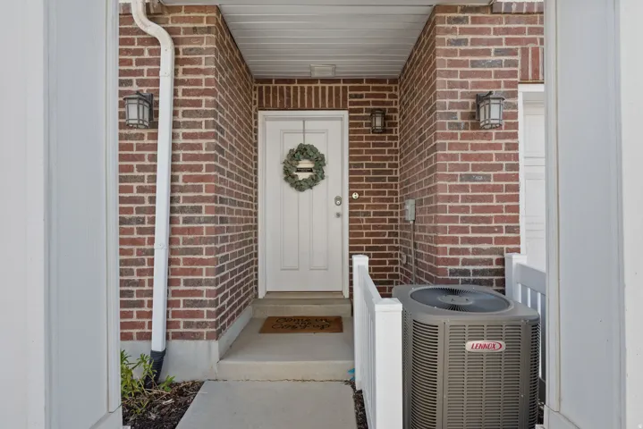 Brick facade entry with a white paneled door, concrete porch, white column, and dual wall-mounted light fixtures