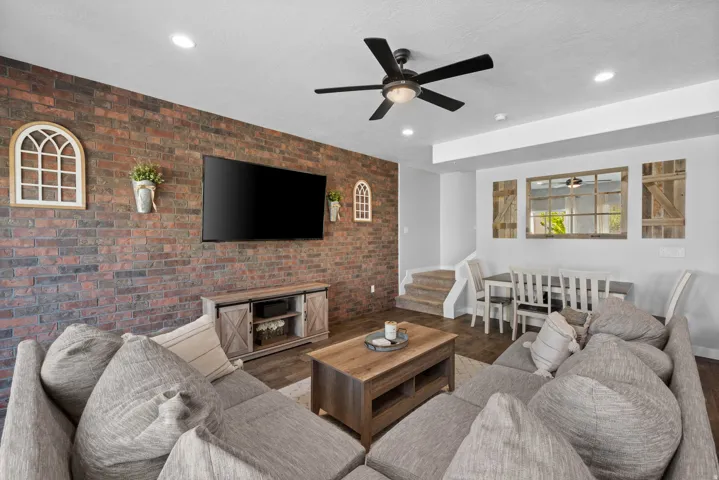 Exposed brick-style accent wall, wood-finish flooring, recessed lighting, and a ceiling fan