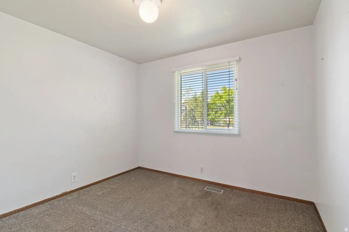 Carpeted room with white walls, a single window featuring horizontal blinds, and a flush-mount ceiling light fixture