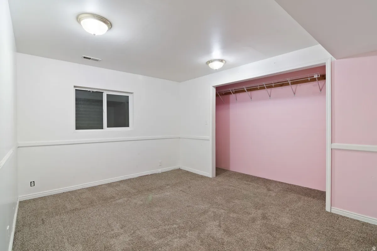 Carpeted room featuring a single window, white baseboards, and a built-in closet with a hanging rod