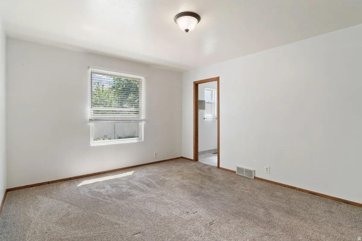 Carpeted room featuring white walls, a single window with blinds, and a flush-mount ceiling light fixture