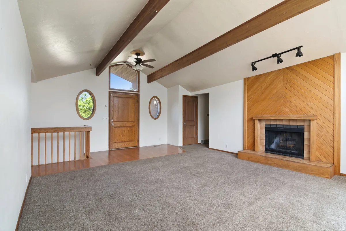 Spacious room featuring vaulted ceilings with exposed wood beams, a wood-finish entry door with transom window, and two oval windows