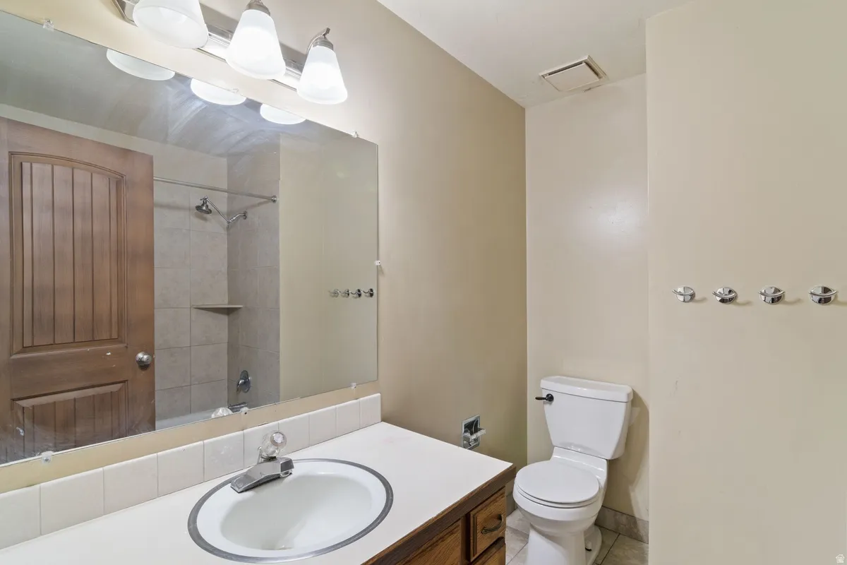 Bathroom featuring a wood-finish vanity with an integrated sink, a large wall-mounted mirror, and a tiled shower with a built-in shelf