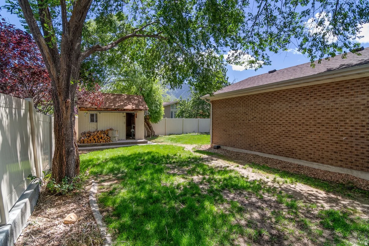 Expansive backyard featuring a detached storage shed with a shingle roof, a privacy fence, and mature trees providing natural shade