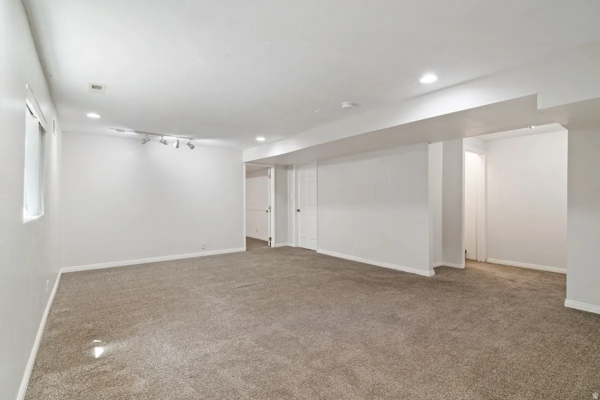 Spacious room featuring neutral carpeting, white walls, recessed lighting, and a track lighting fixture