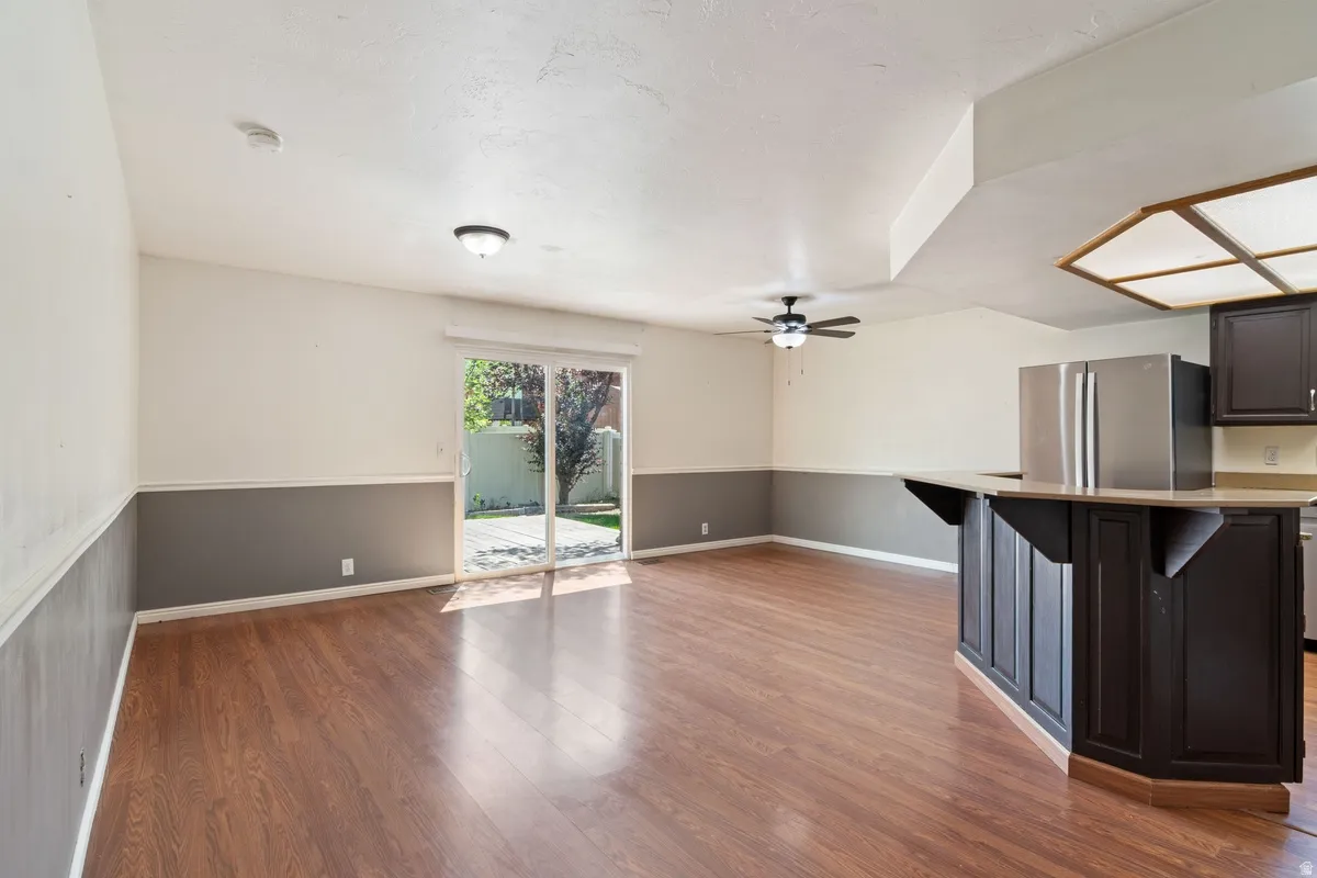 Open-concept living area featuring wood-finish flooring, two-tone wall treatment, ceiling fan, and sliding glass door access to the exterior
