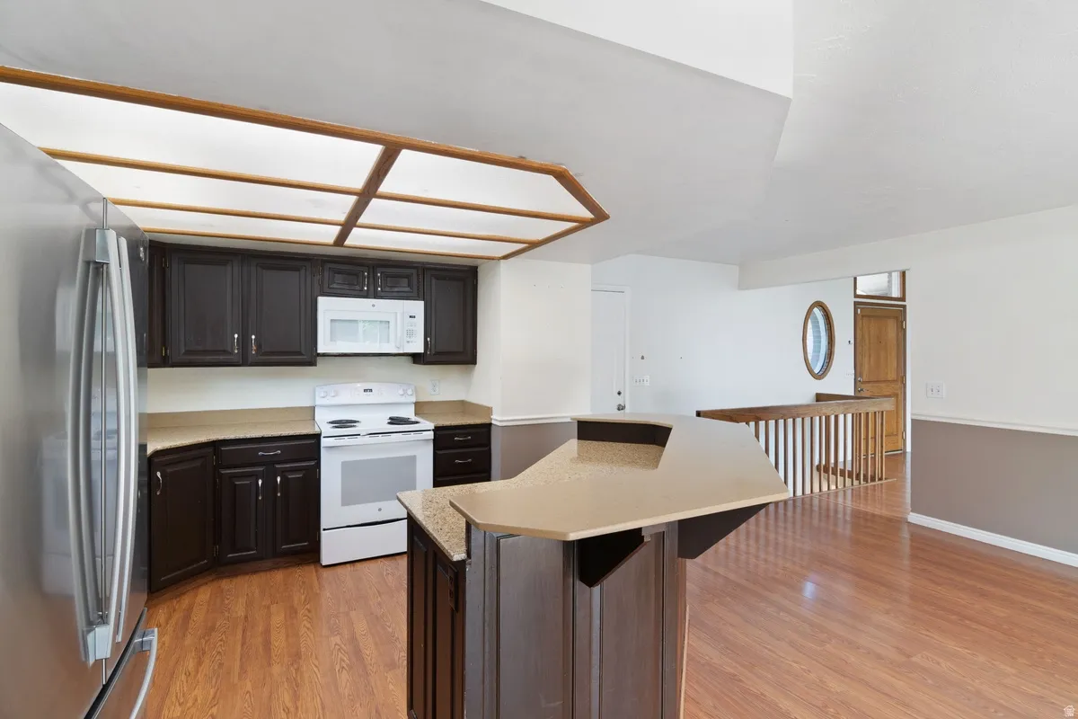 Kitchen featuring dark wood cabinetry, light countertops, and white appliances