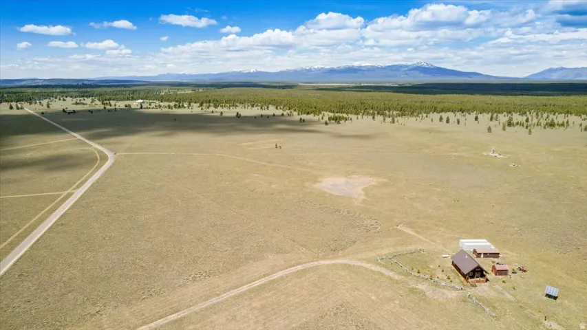 Expansive open land featuring a residence with a brown roof, multiple outbuildings, and a mountainous backdrop