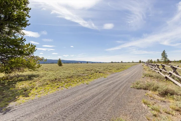 Expansive open land featuring a gravel road, split-rail fence, and mature evergreen trees