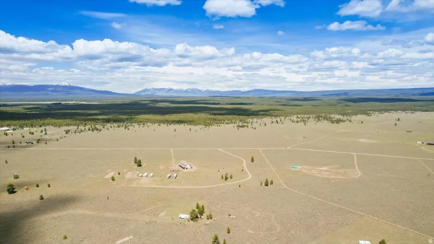 Expansive land parcel featuring multiple structures, open fields, scattered evergreen trees, and distant mountain ranges