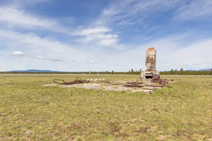 Stone and brick chimney structure on a concrete foundation, surrounded by an expansive grass field
