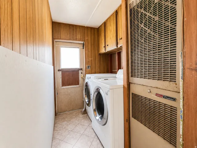 Utility space featuring wood-finish paneling, a white painted wall, and light-toned tile flooring
