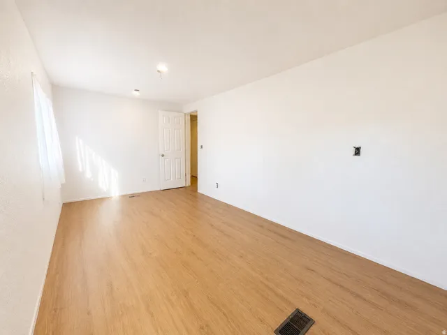 Spacious room with wood-finish flooring, white walls, and a multi-panel interior door
