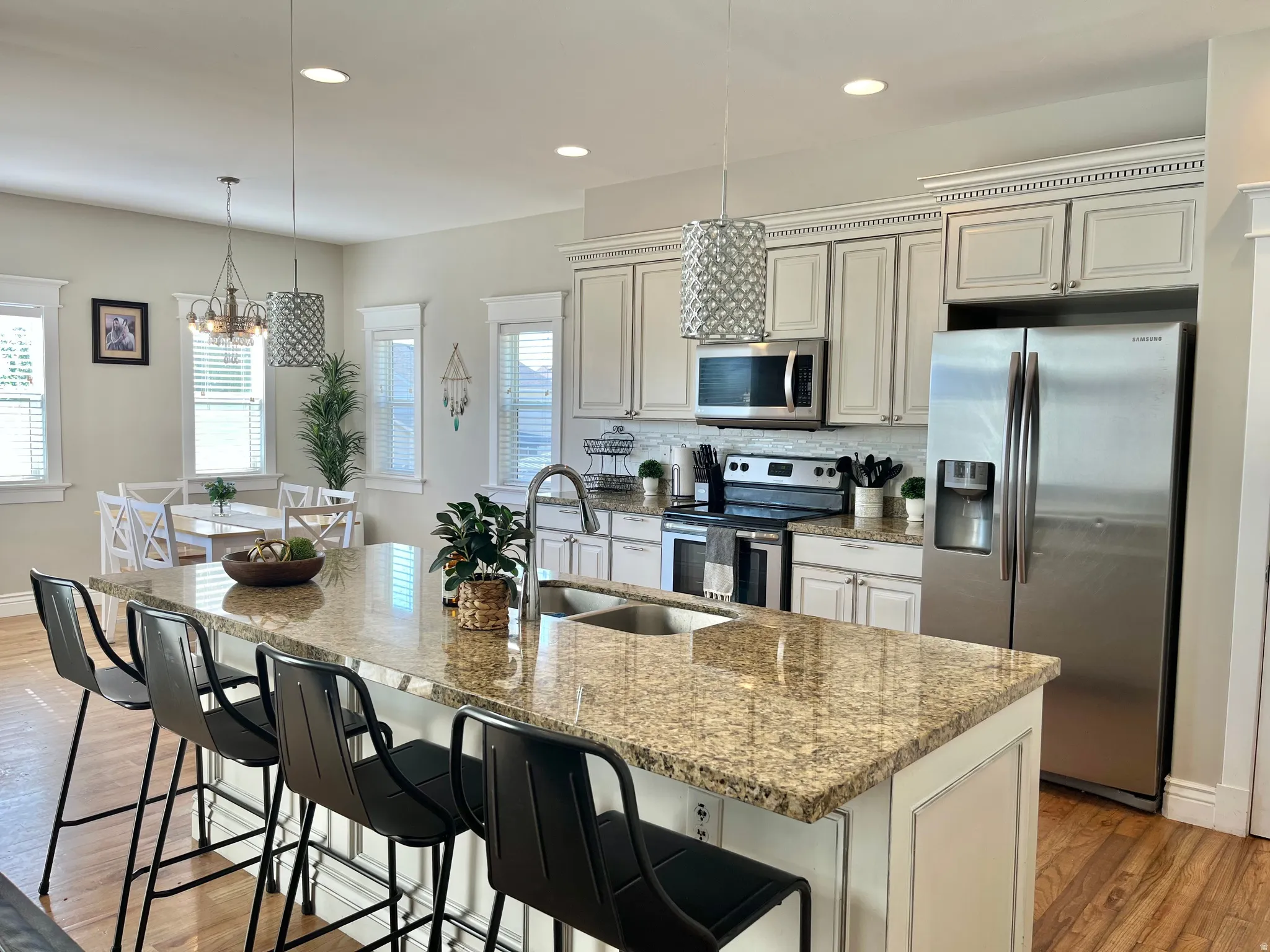 Spacious kitchen featuring an expansive island with granite countertops, stainless steel appliances, light-toned cabinetry, wood-finish flooring, and recessed lighting