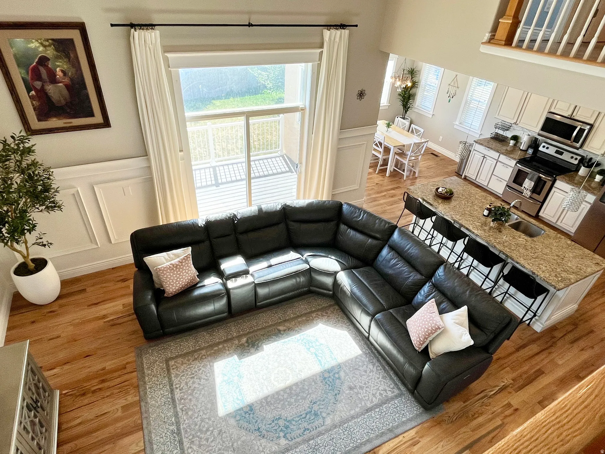 Open-concept living area featuring wood-finish flooring and a kitchen with white cabinetry, stainless steel appliances, and a granite-look island with seating
