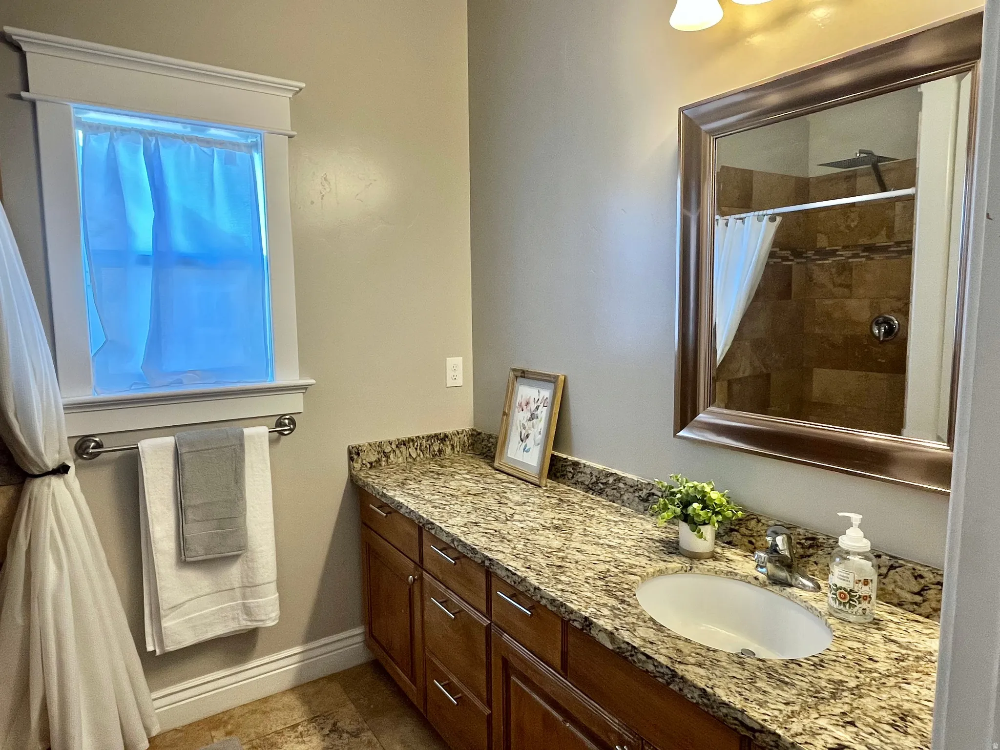 Bathroom vanity featuring a granite countertop with an undermount sink, warm wood-finish cabinetry, and a framed mirror