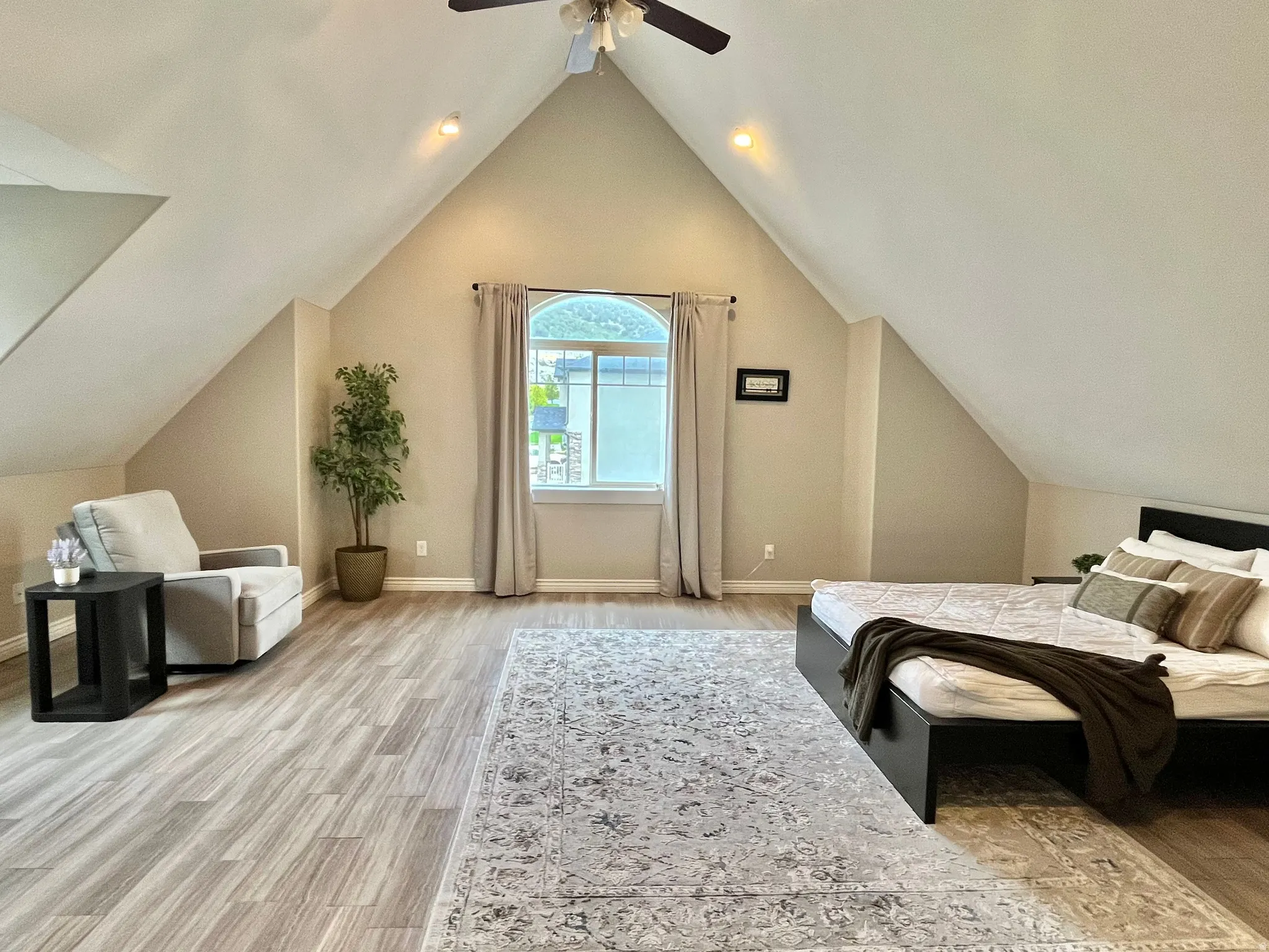 Spacious  master bedroom featuring vaulted ceilings, wood-finish flooring, an arched window, and a ceiling fan with integrated lighting