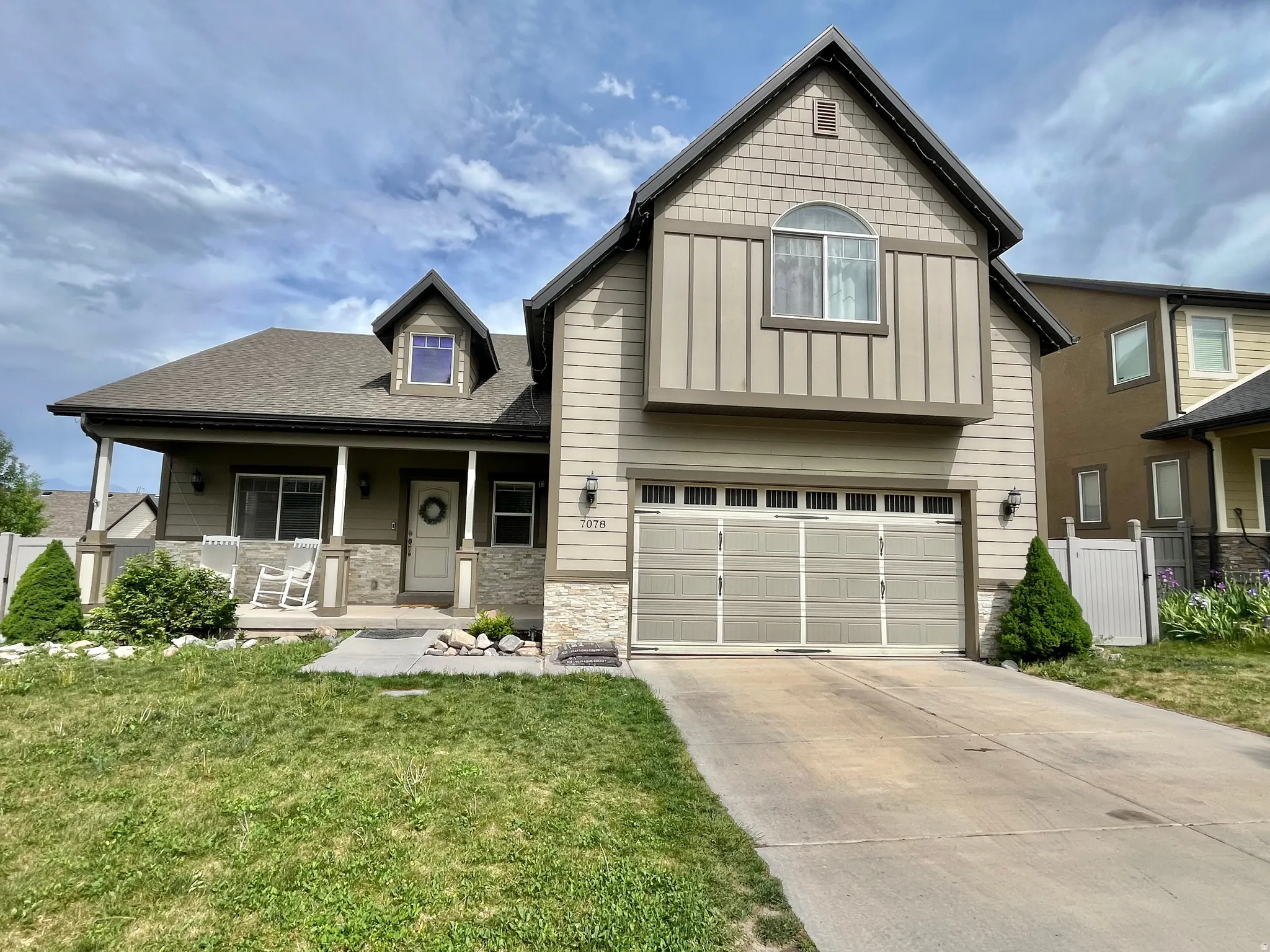 Property exterior featuring a covered porch, stone accents, two-car garage, and a dormer window