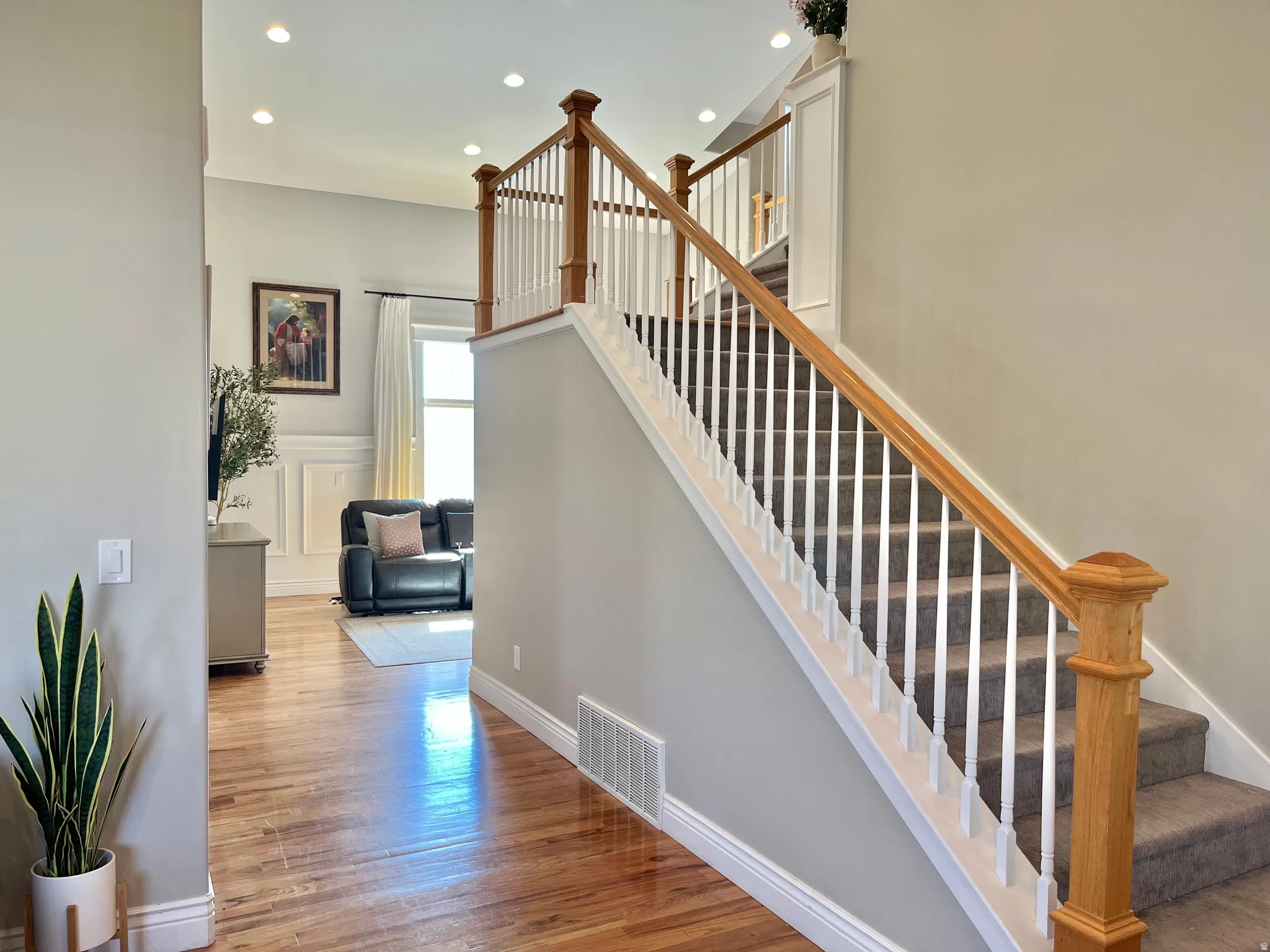 Inviting entryway featuring hardwood flooring, a carpeted staircase with wood and white balusters, recessed lighting, and white baseboards