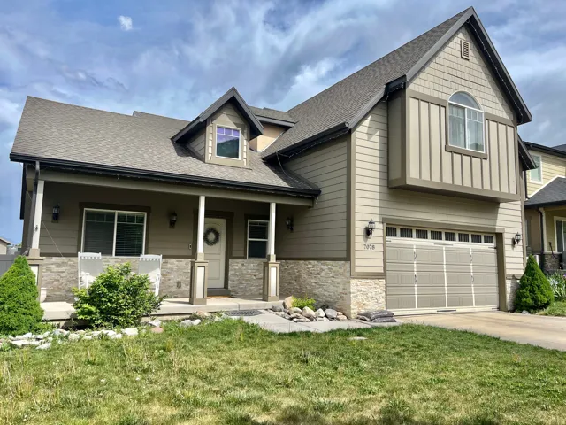 Contemporary two-story residence featuring a two-car garage, covered front porch, stone veneer accents, dormer window, and shingle siding