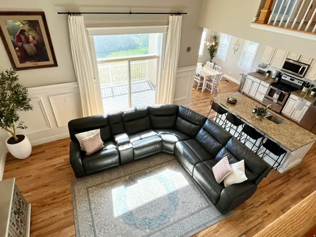 Open-concept living area featuring wood-finish flooring and a kitchen with white cabinetry, stainless steel appliances, and a granite-look island with seating